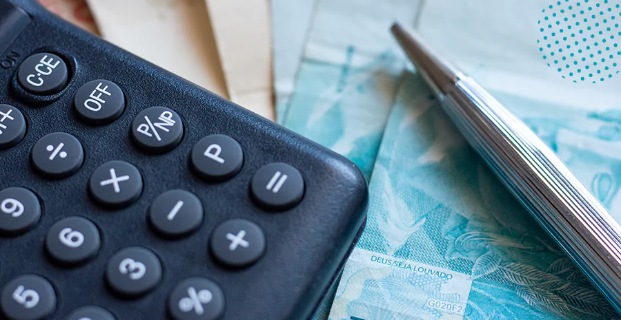 imagem de uma calculadora ao lado de um lápis e de notas de dinheiro