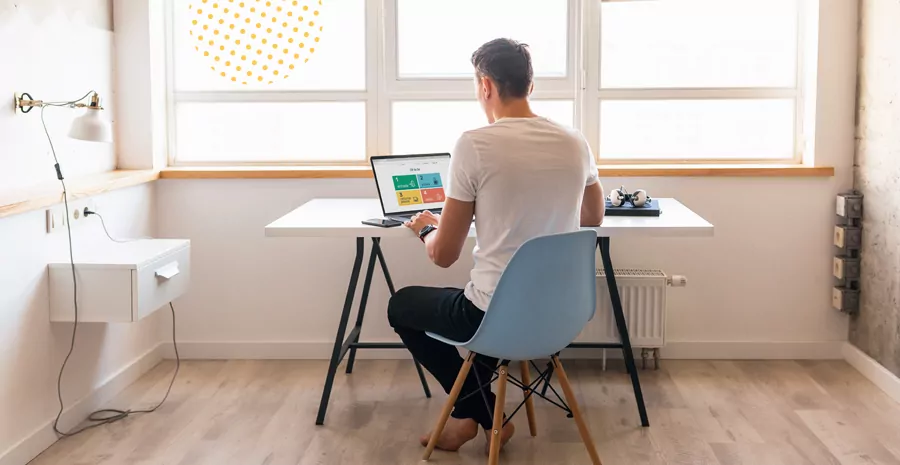 imagem de um homem sentado em frente a uma janela mexendo em um computador, representando o controle de ponto home office