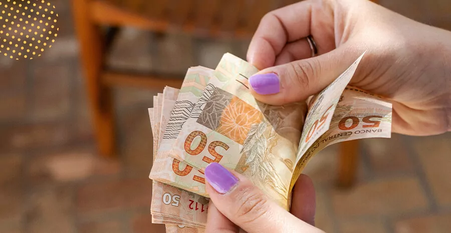 Mãos contando notas de 50 reais para pagamento de adicional de transferência