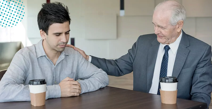 imagem de um homem mais velho e um homem mais novo sentados em uma mesa com copos de café 