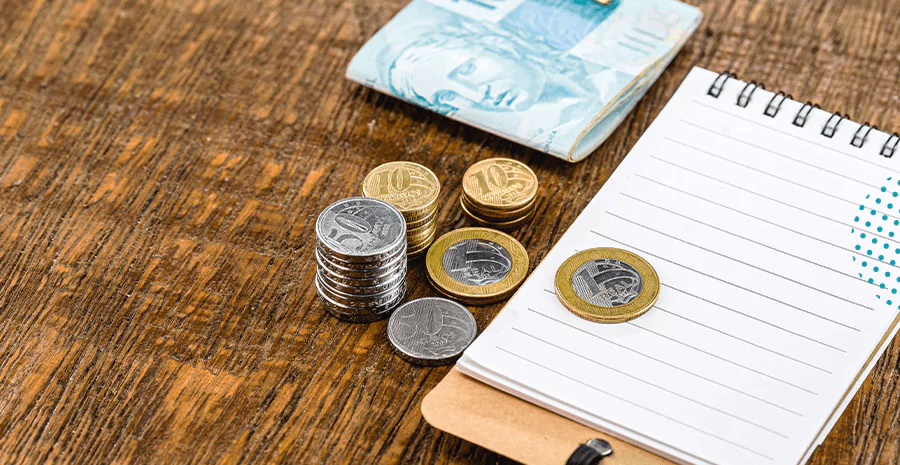 imagem de umas moedas e nota de cem reais sobre uma mesa