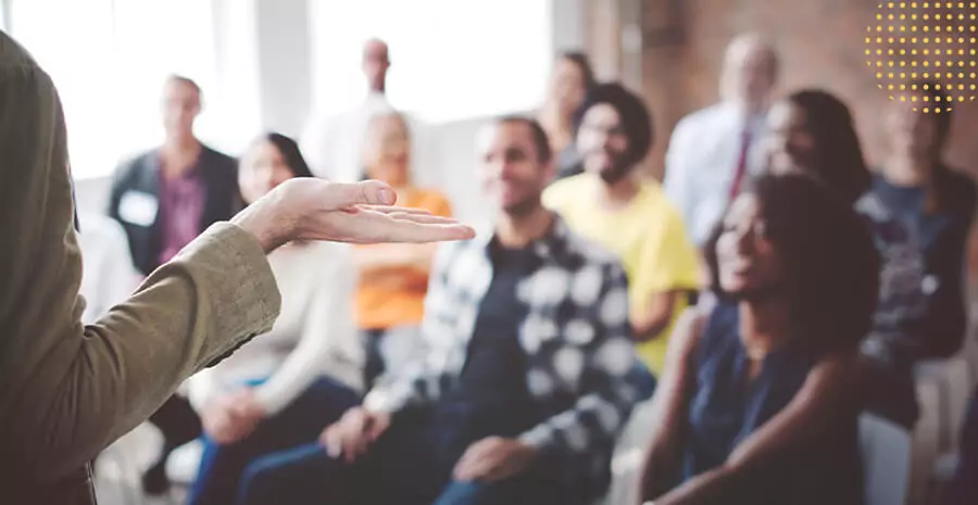 imagem de uma mulher dando aula ou palestras para um grupo de jovens. 