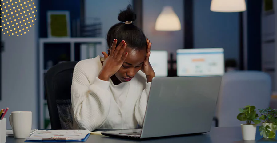 imagem de uma mulher sentada de frente para um computador com uma aparência de desmotivação no trabalho e estresse, representando desmotivação no trabalho