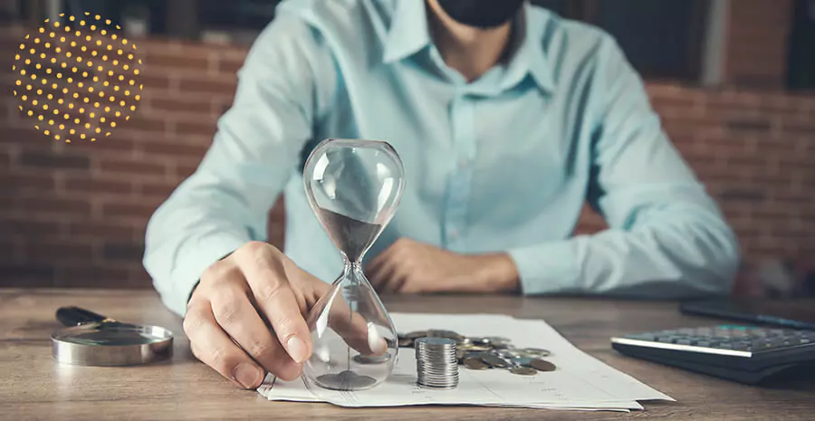 um homem de camisa azul clara sentado em uma mesa, na frente dele há uma ampulheta