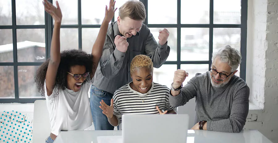 imagem de um grupo, homens e mulheres, em volta de um computador, todos olham para o pc e vibram