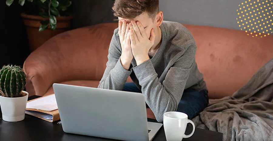 imagem de um homem sentado no sofá em frente uma mesa com notebook, com as mãos no rosto preocupado com a demissão remota