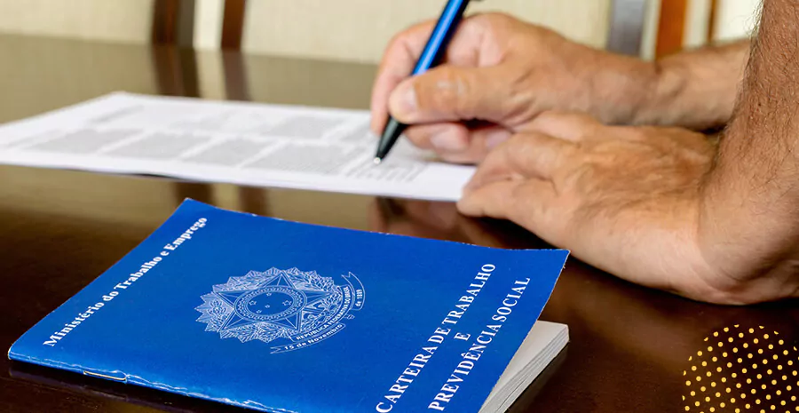 imagem de uma carteira de trabalho sob uma mesa e uma pessoa assinando em um papel