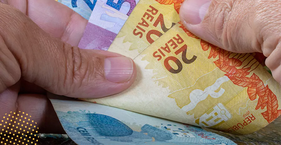imagem de uma mão segurando algumas cédulas de dinheiro do salário mínimo
