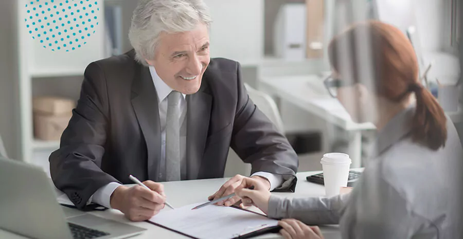 imagem de um homem de cabelo branco vestindo terno sentado em uma mesa de frente para uma mulher