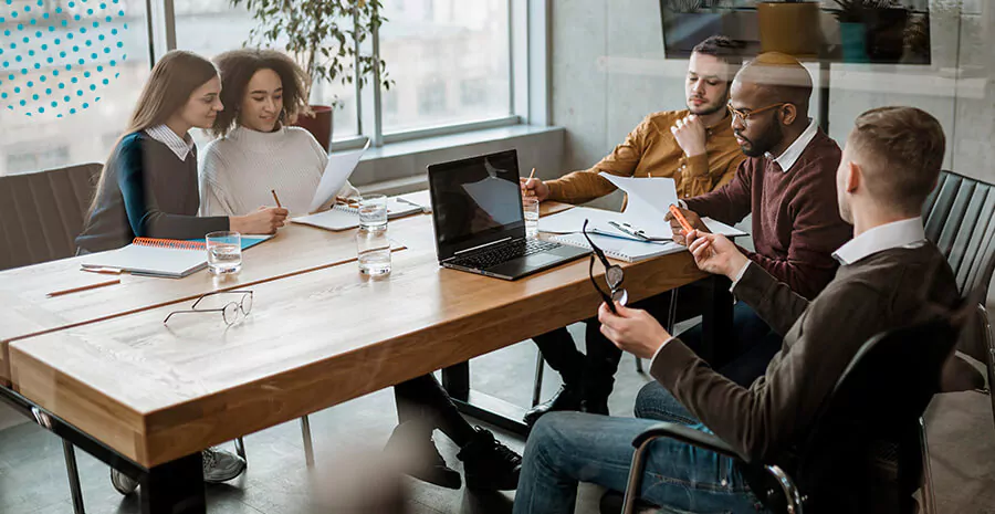 imagem de 5 pessoas trabalhando em uma mesa grande 