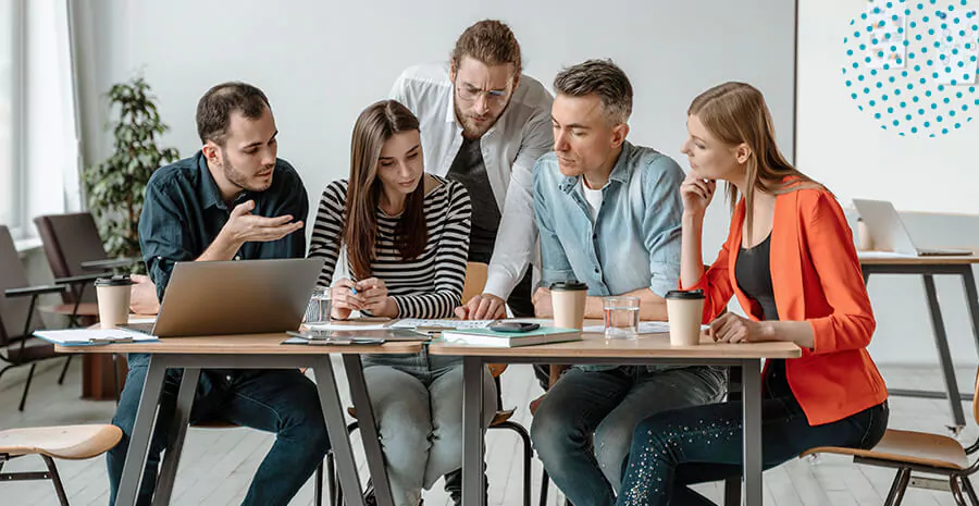 imagem de uma equipe de trabalho conversando trabalhando em conjunto em frente uma mesa com notebook papéis, cadernos etc