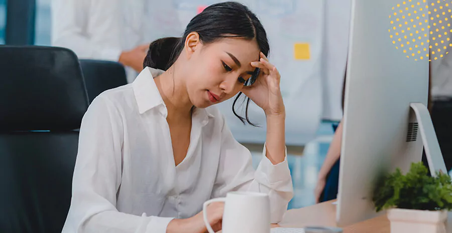 imagem de uma mulher sentada de frente para um computador com o braço apoiado na mesa pensando com expressão de preocupada