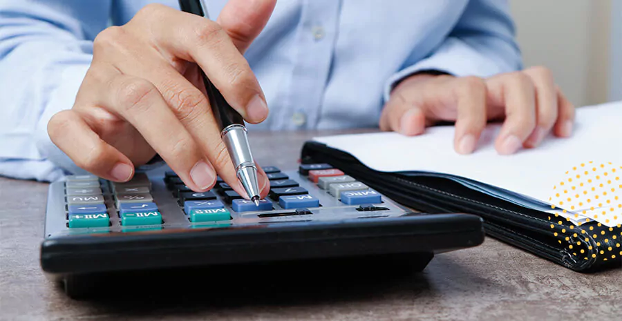 imagem de uma pessoa mexendo numa calculadora segurando uma caneta sob a mesa e ao lado uma pasta com papéis em cima