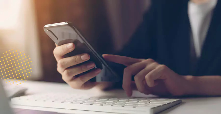 imagem de uma pessoa segurando um celular apoiado em uma mesa com um teclado de computador