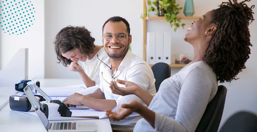 imagem de três pessoas trabalhando sentadas em frente a uma mesa com notebook sorrindo e felizes