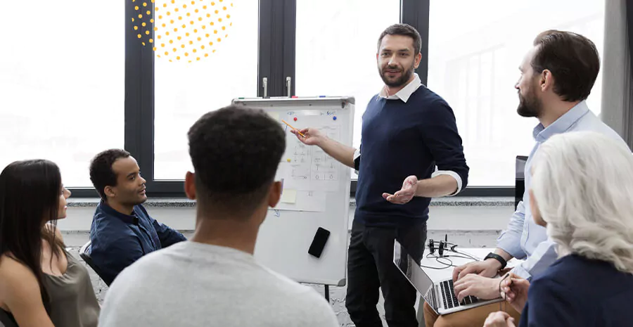 imagem com diversas pessoas e um homem no centro apontando para um flipchart