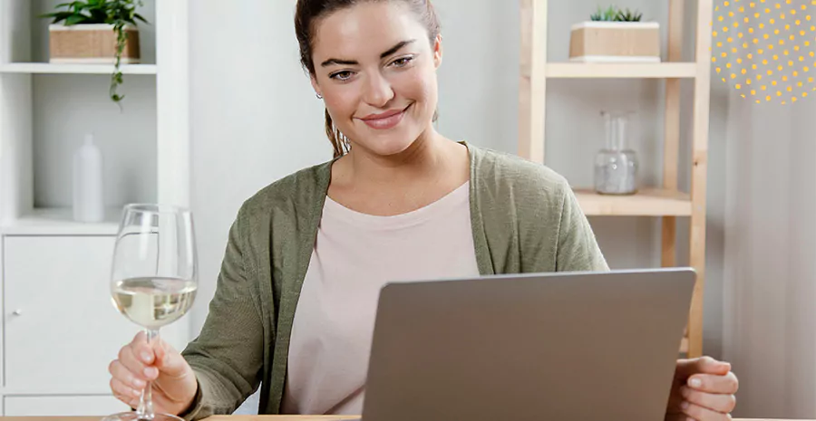 imagem de uma mulher sentada na frente do computador segurando uma taça de vinho