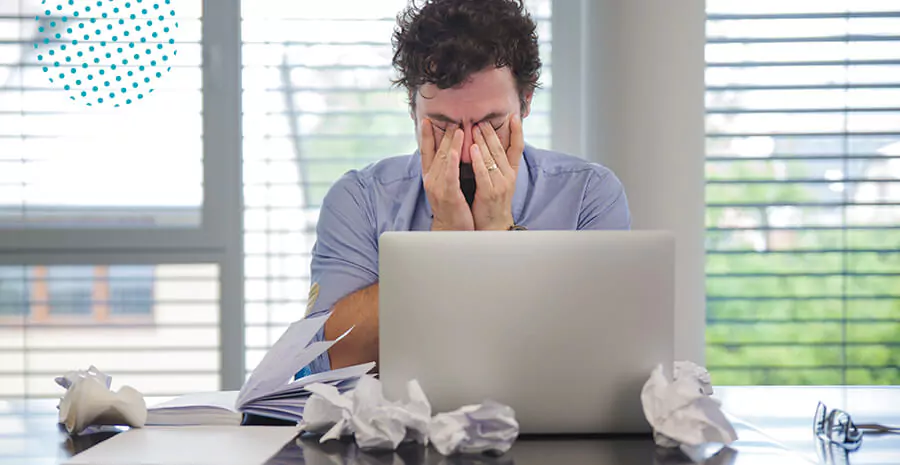 imagem de um homem estressado na frente de um computador com as mãos no olho