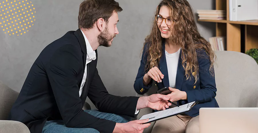 imagem de um homem e uma mulher sentados do lado um do outros conversando e segurando uma prancheta