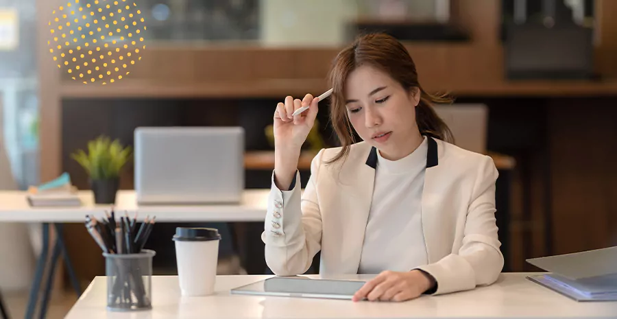 imagem de uma mulher sentada olhando para um tablet e segurando uma caneta ao lado da cabeça