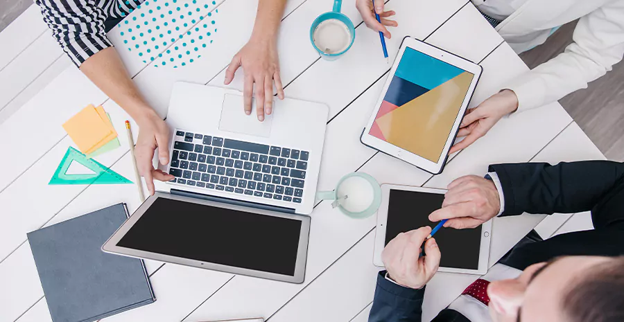 imagem de duas pessoas sentadas em uma mesa mexendo no computador e tablets