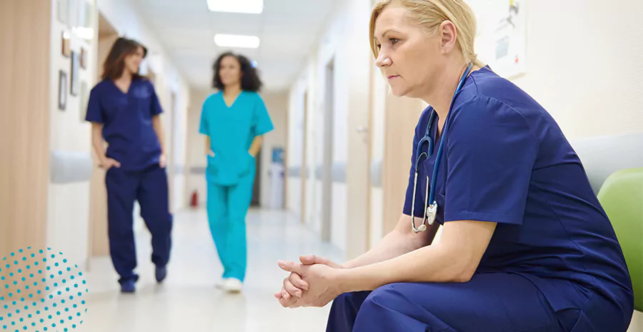 imagem de uma médica sentada com cara de cansada no corredor com duas outras médicas andando atrás 