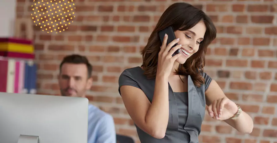 imagem de uma mulher falando ao telefone e um homem atras mexendo no computador