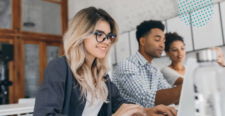 imagem de uma mulher sorrindo mexendo no computador com dois colegas ao lado conversando