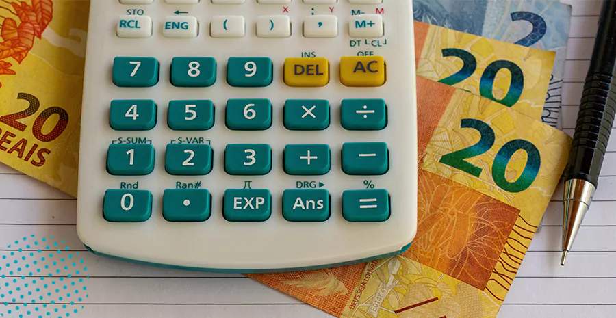 imagem de uma calculadora ao lado de uma caneta e em cima de notas de vinte reais e de dois reais