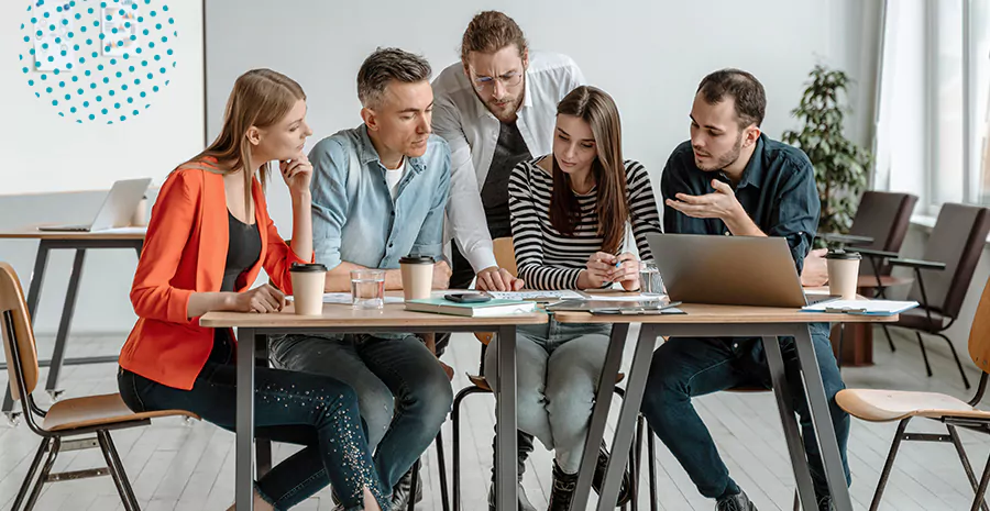 imagem de três mulheres e dois homens sentados em uma mesa conversando e olhando para folhas de papel na mesa