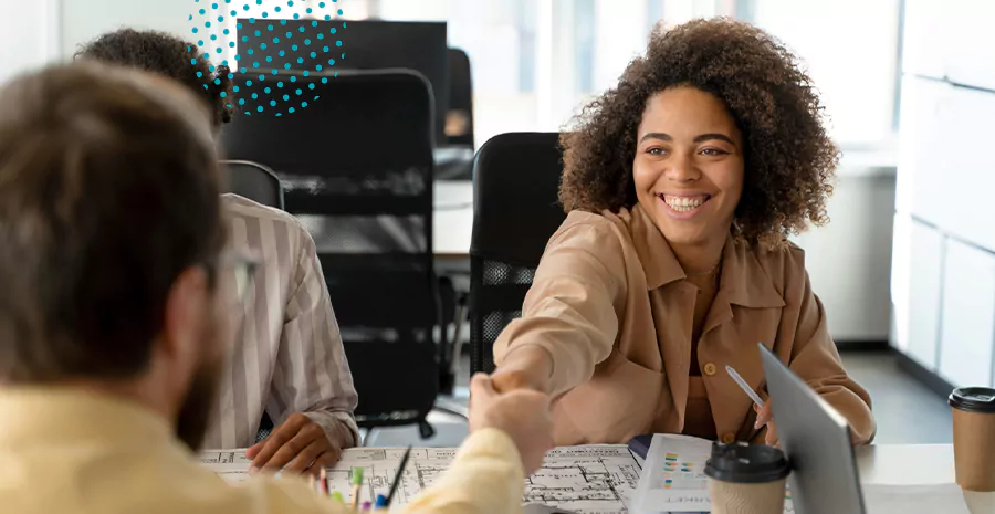 imagem de uma mulher sorrindo cumprimentando um homem sentado na outra ponta de uma mesa
