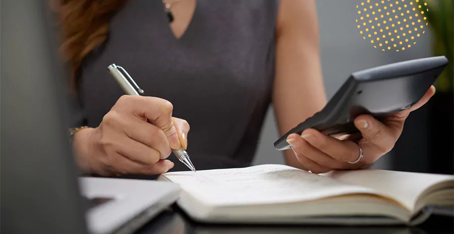 imagem de uma mulher segurando uma calculadora e anotando em um caderno