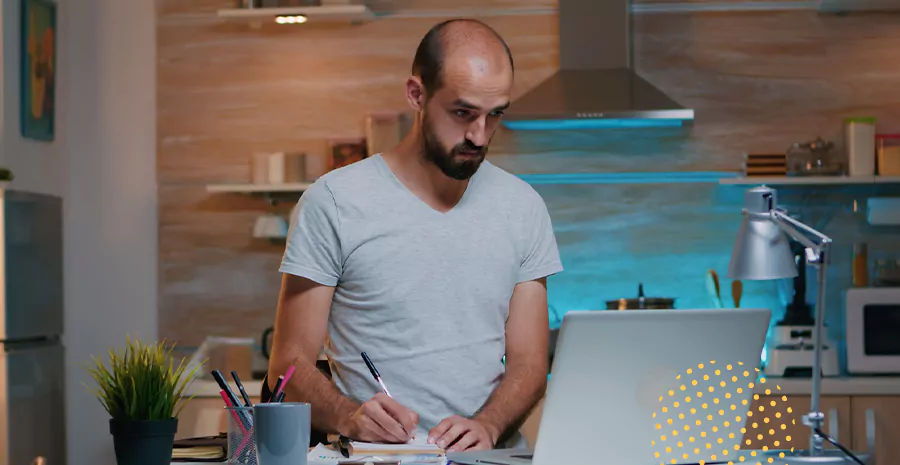 imagem de um homem olhando para um computador e escrevendo em um caderno