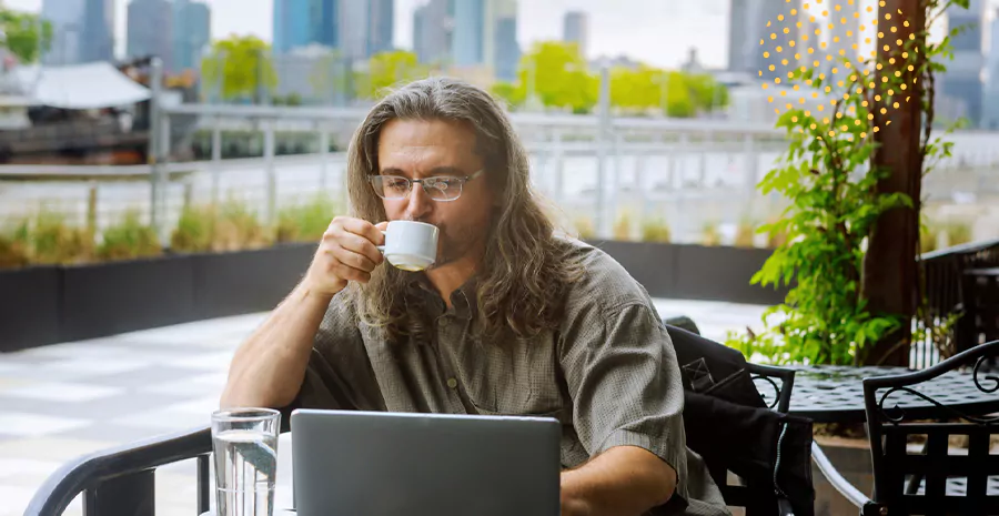 imagem de um homem sentado na frente de um computador bebendo em uma xícara 