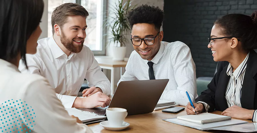 imagem de dois homens e duas mulheres sentados ao redor de uma mesa conversando e mexendo em um computador