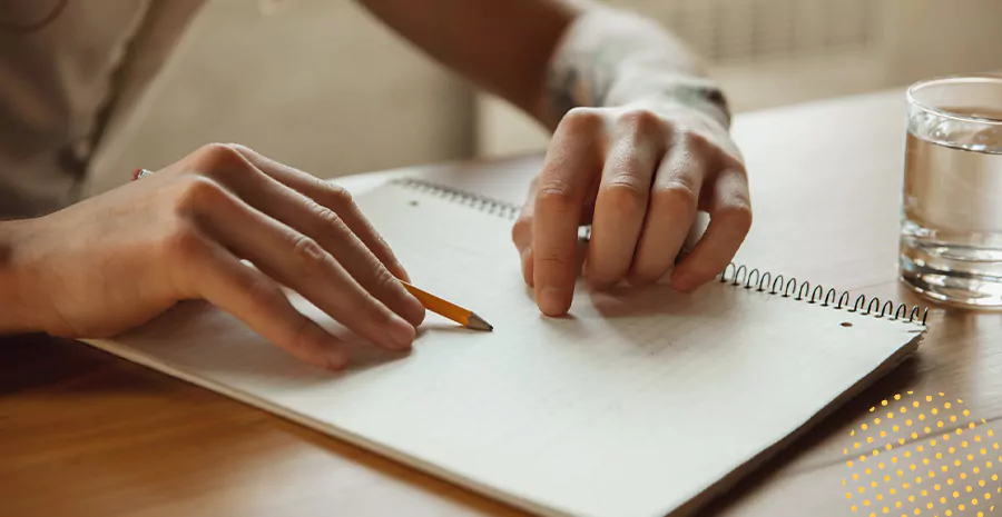 imagem de uma pessoa sentada em uma mesa escrevendo em um caderno