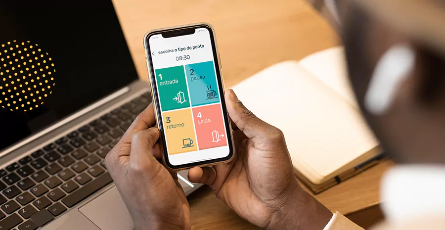 imagem de uma pessoa sentada na frente de um computador e segurando um celular usando o aplicativo de controle de ponto da pontotel