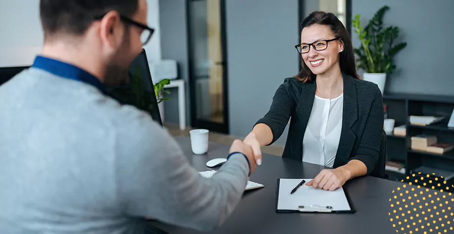 imagem de um homem e uma mulher sentados em lados opostos de uma mesa sorrindo e se cumprimentando