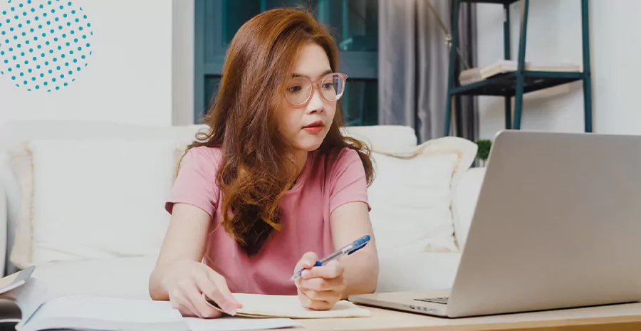 imagem de uma mulher sentada na frente de um computador escrevendo em um caderno