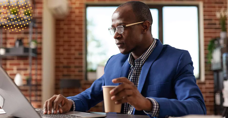 imagem de um homem segurando um café sentado na frente de um computador