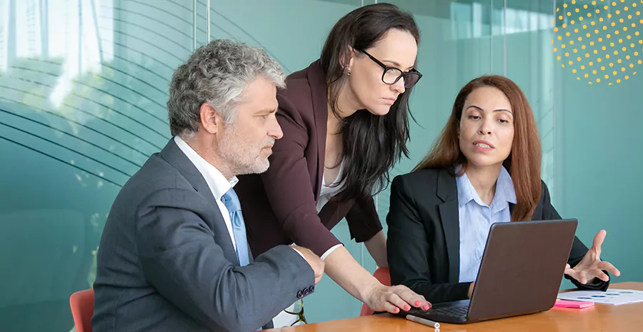 imagem de duas mulheres e um homem olhando para um computador em cima de uma mesa