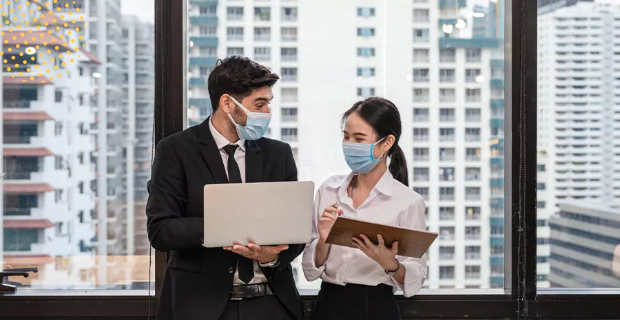 imagem de um homem e uma mulher em pé usando máscaras de proteção e segurando tablets