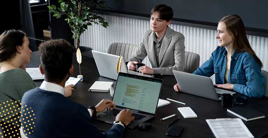 imagem de duas mulheres e dois homens sentados ao redor de uma mesa conversando e mexendo em computadores