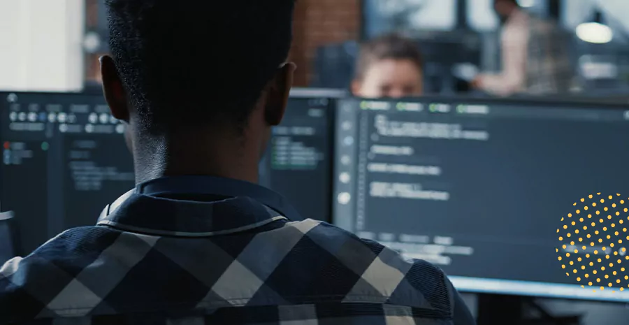 imagem de um homem sentado na frente de dois computadores