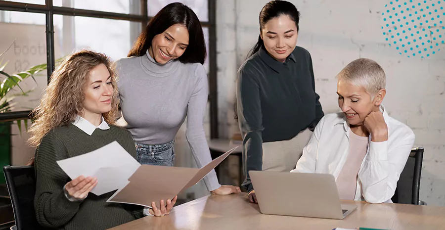 imagem de quatro mulheres ao redor de uma mesa conversando e olhando para papéis e um computador