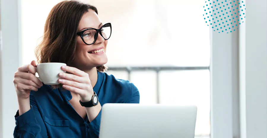 imagem de uma mulher sentada na frente de um computador sorrindo e segurando uma xícara