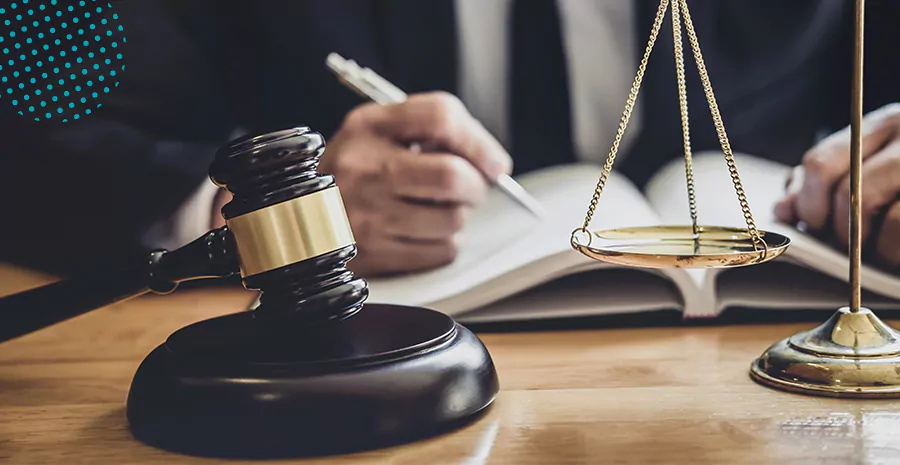 imagem de um homem escrevendo em um livro ao lado de um martelo de juiz e uma balança em cima da mesa