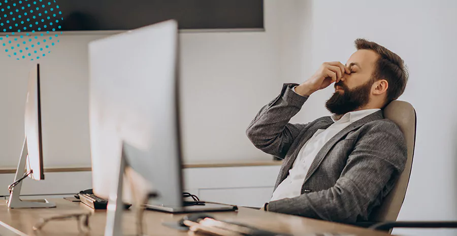 imagem de um homem sentado na frente de um computador cansado colocando a mão nos olhos