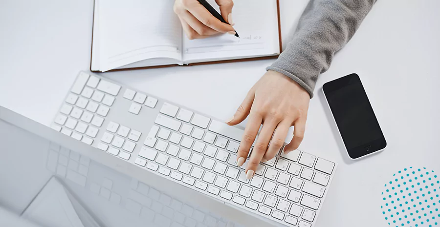 imagem de uma pessoa escrevendo em um caderno e digitando em um teclado
