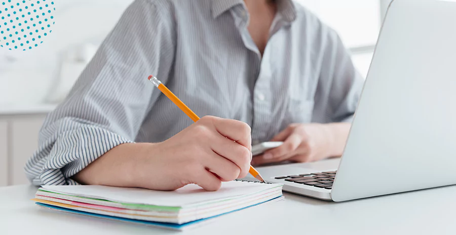 imagem de uma pessoa sentada na frente de um computador escrevendo em um caderno